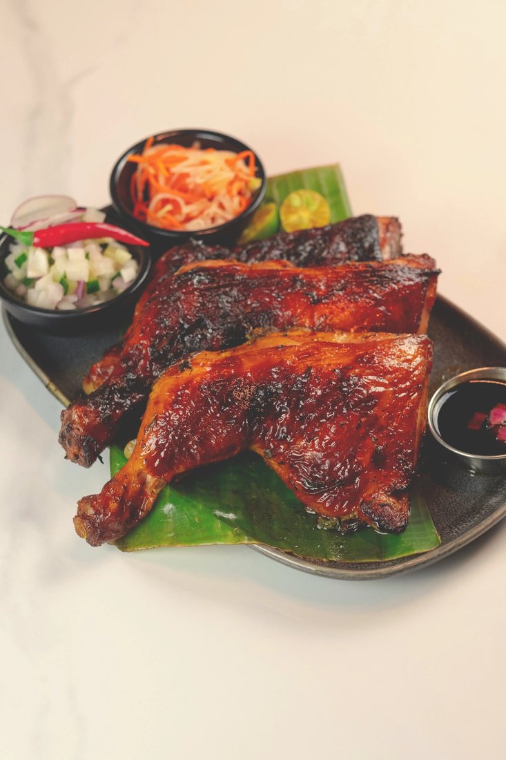 Grilled Chicken Inasal with atchara and dipping sauces on a banana leaf
